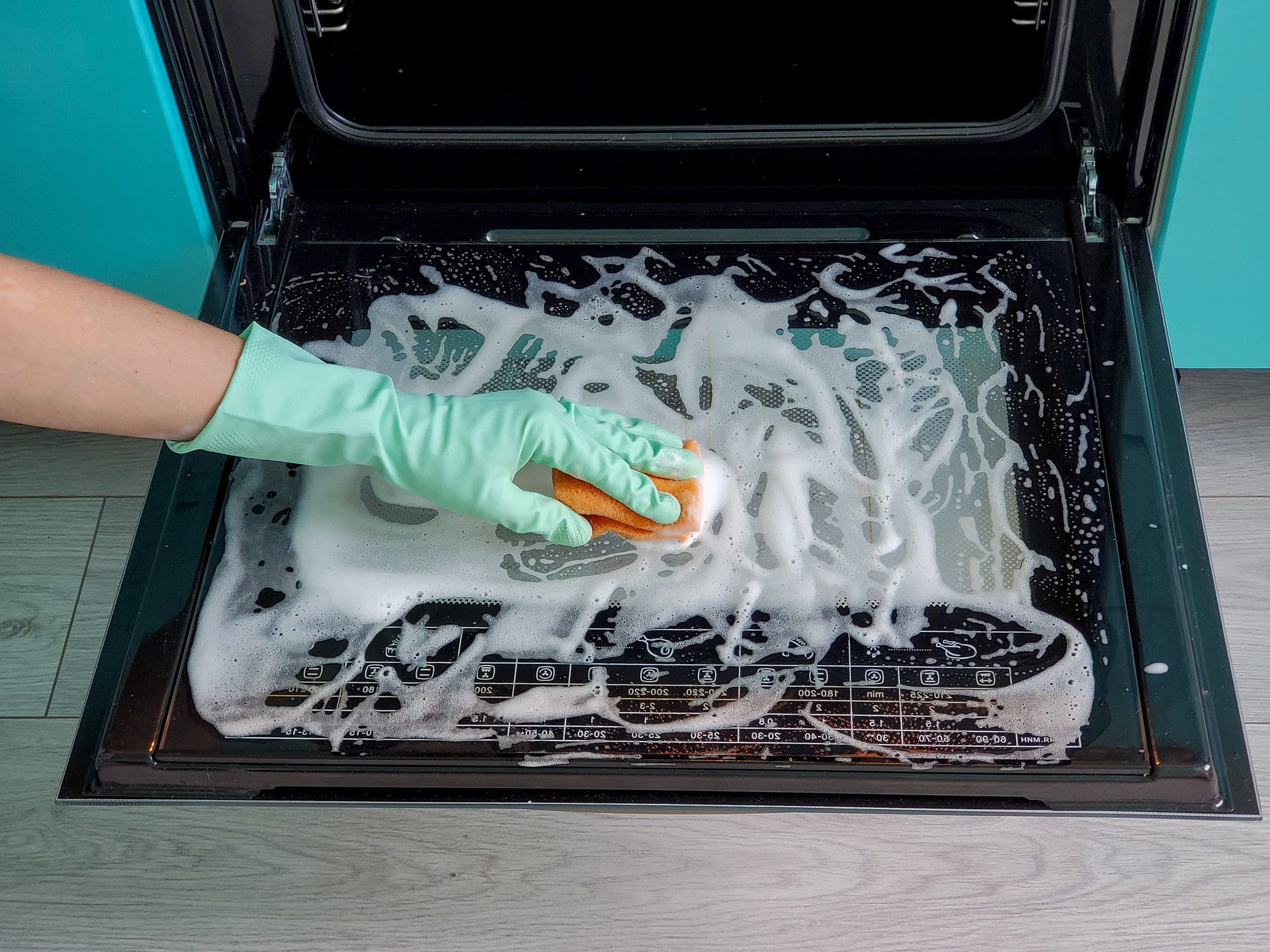 women's hands in gloves using a sponge and detergent cleans the oven door